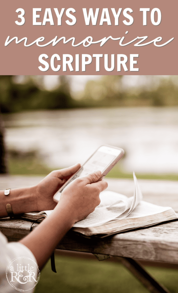 person sitting at table outside with Bible holding cell phone