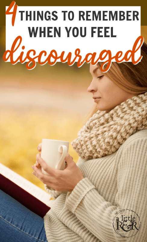 woman in sweater and ripped jeans sitting against a tree drinking coffee and reading