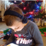 boy sitting in front of a Christmas tree and watching a reading of The Snowy Day book on YouTube
