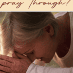 woman with head on folded hands bowed over a Bible praying